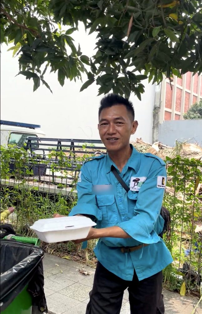 Seorang pekerja berseragam biru tersenyum sambil memegang nasi kotak