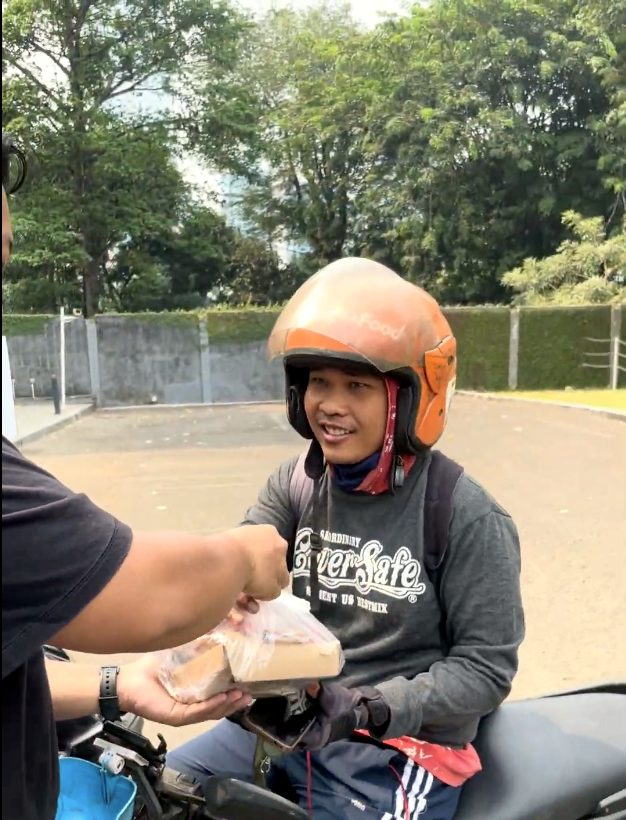Pengemudi ojek daring berhelm oranye tersenyum saat menerima nasi kotak dari tangan relawan