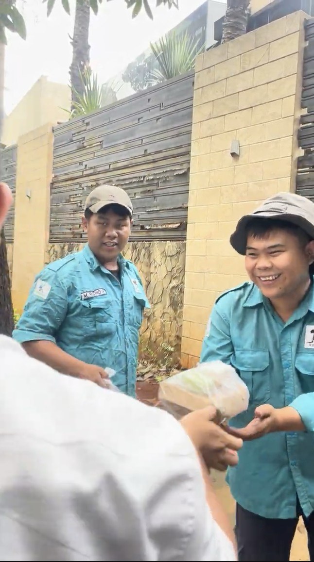 Dua petugas berseragam menerima bungkus nasi sambil tersenyum